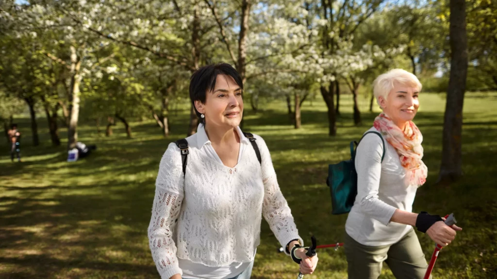 Dos mujeres mayores de 45 años practicando marcha nórdica por el bosque para mejorar fuerza, movilidad y bienestar